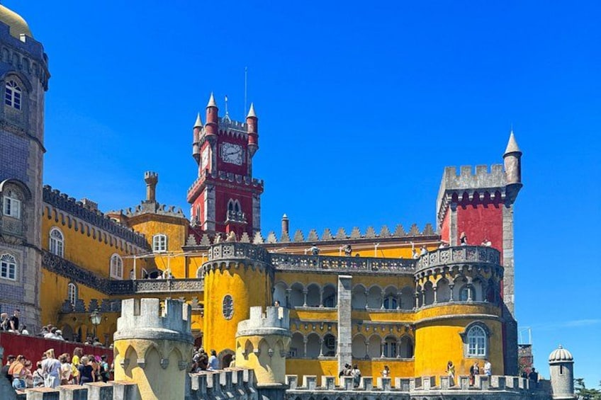 Un castello storico con mura gialle e rosse, una torre dell'orologio e un cielo azzurro intenso. 3