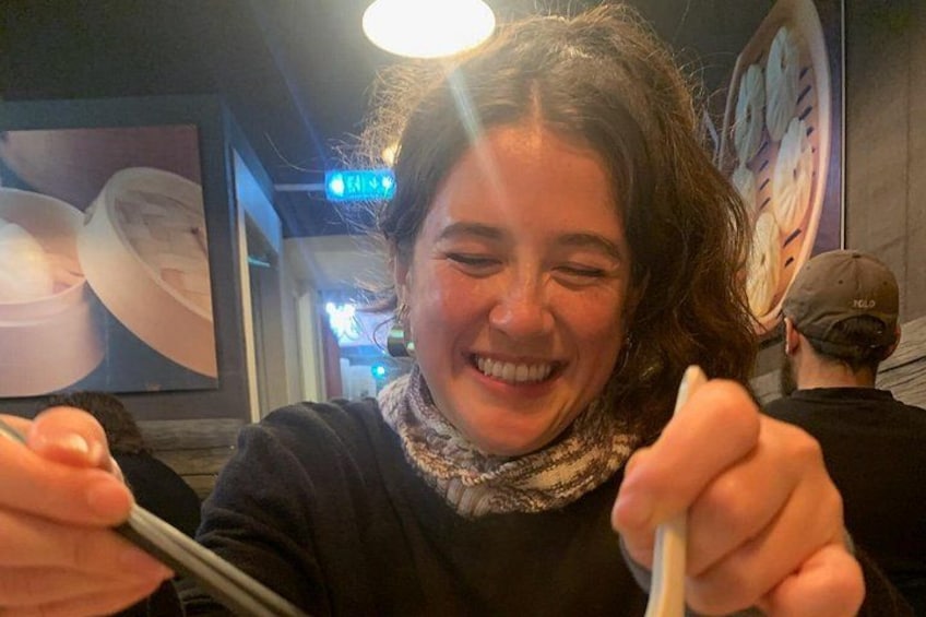 Une personne tenant des baguettes, assise à l’intérieur, avec un menu à la main, et un mur sur lequel est affichée une grande image de pizza en arrière-plan. 4