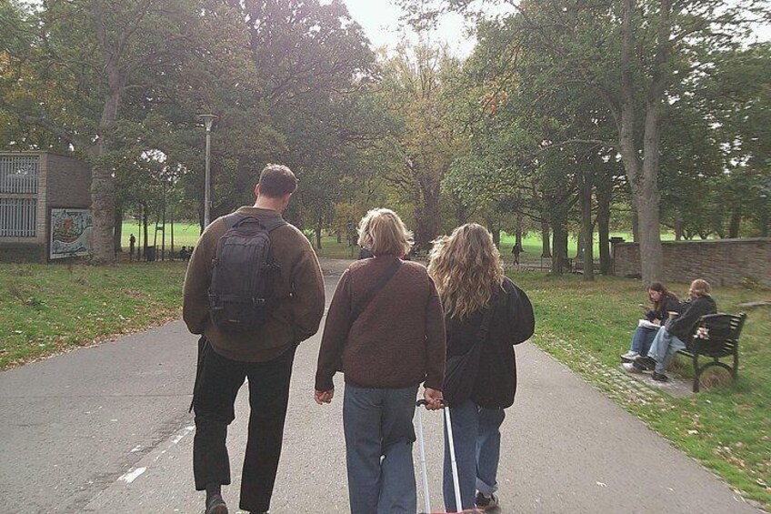 Three people walking on a paved path in a park with trees and a bench in the background. 4