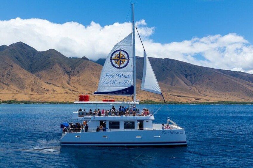 A sailboat with a star emblem on its sail, named 'Four Winds,' on a calm lake with mountains in the background. 1