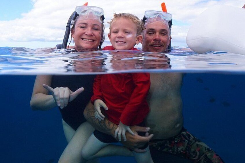 Una persona con traje de neopreno negro sostiene a un niño con traje rojo, ambos con equipo de snorkel, bajo el agua. 2