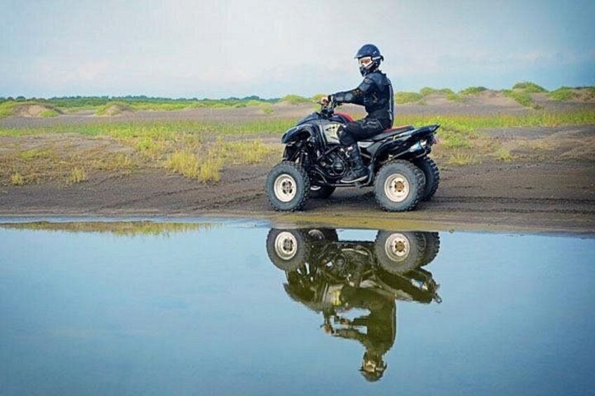 A person on a quad bike near a body of water with a clear reflection. 4