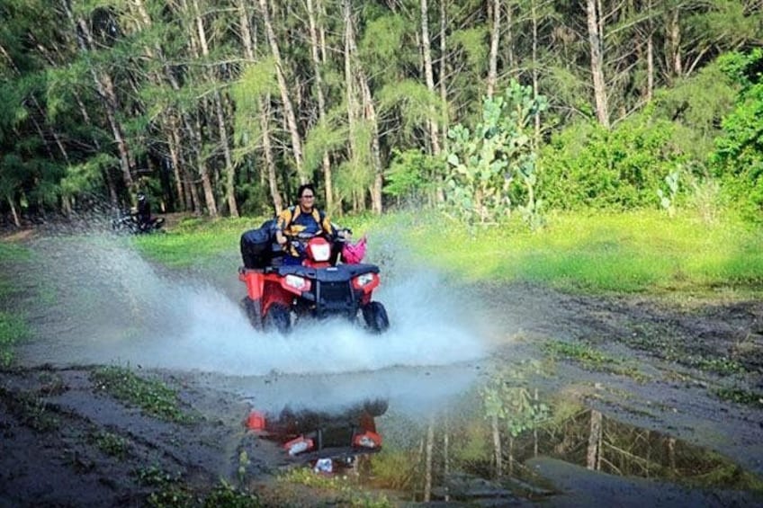 A person riding an ATV through a muddy area with splashes of water. 2