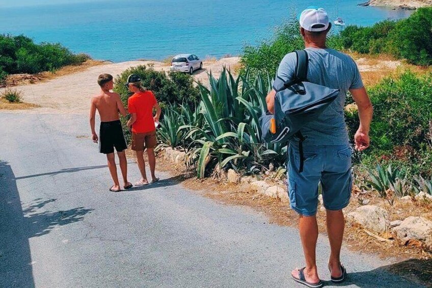 A coastal road with a man walking, two people standing, and a car parked by the beach. 5