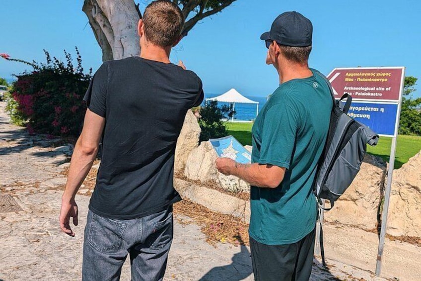 Two people standing near a sign with text, a tree, and a tent in the background. 3