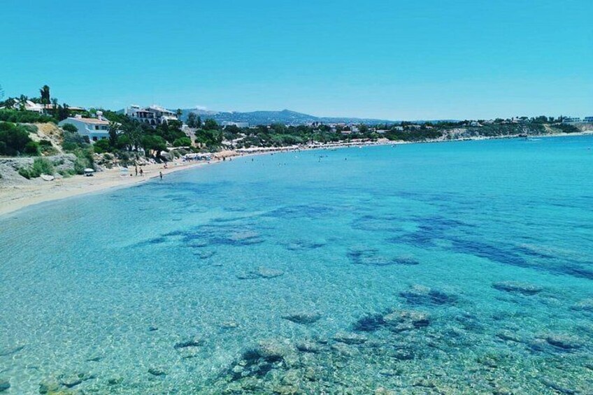 A clear blue sea, a sandy beach, and buildings in the background. 4