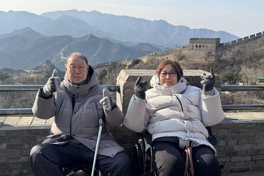 Due persone sedute su un muro con un paesaggio montuoso e la Grande Muraglia Cinese sullo sfondo. 1