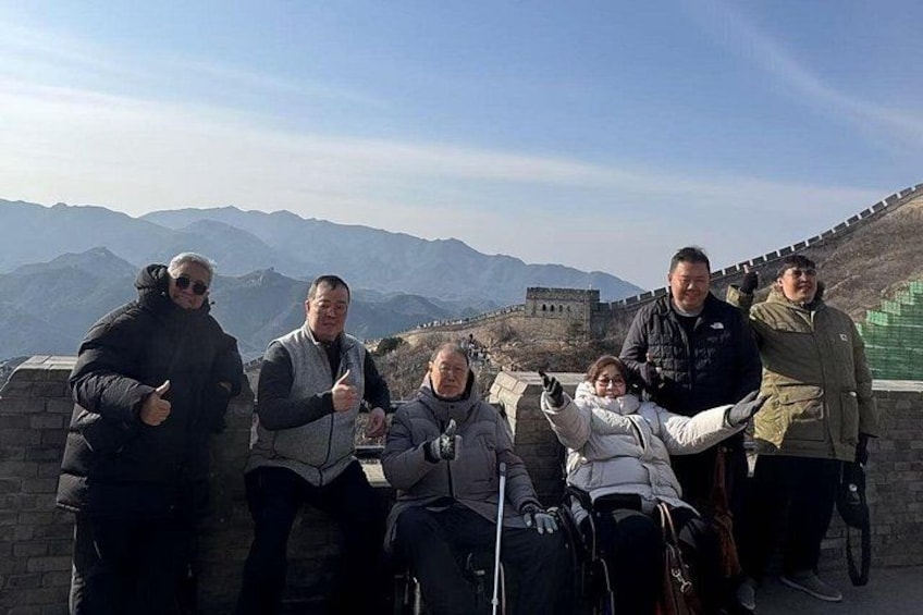 A group of people sitting on a wall overlooking a mountainous landscape with a historical structure in the background. 3