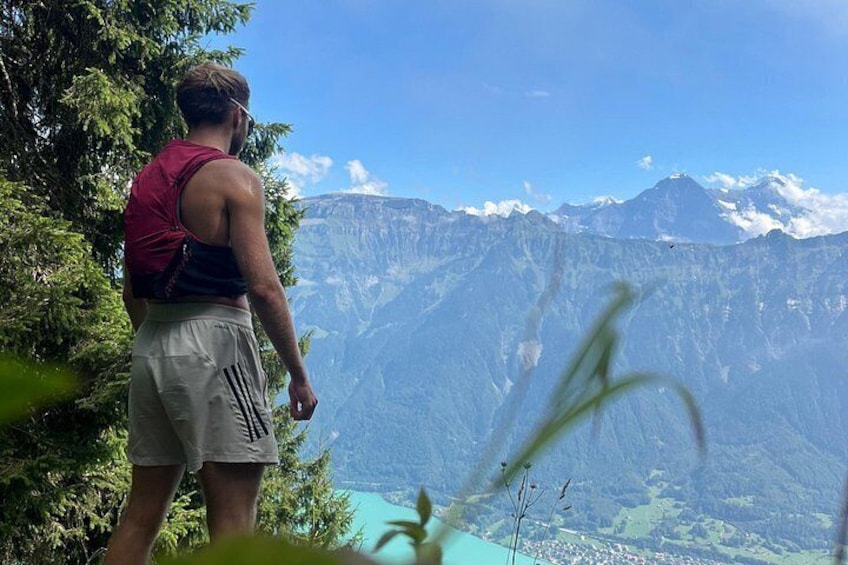 Una persona parada en un sendero de montaña, con vistas a un valle con un lago y montañas al fondo. 5