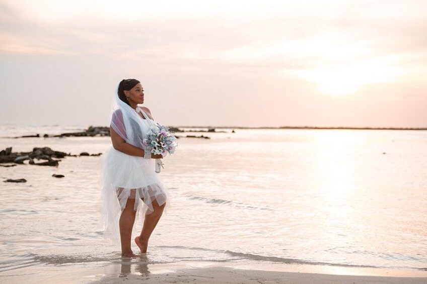 A person standing on a beach holding a bouquet, with the ocean and a sunset in the background. 5