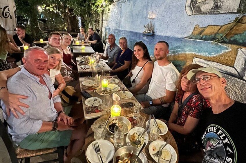 Een groep mensen eet in een openluchtrestaurant met een muurschildering op de achtergrond. 4