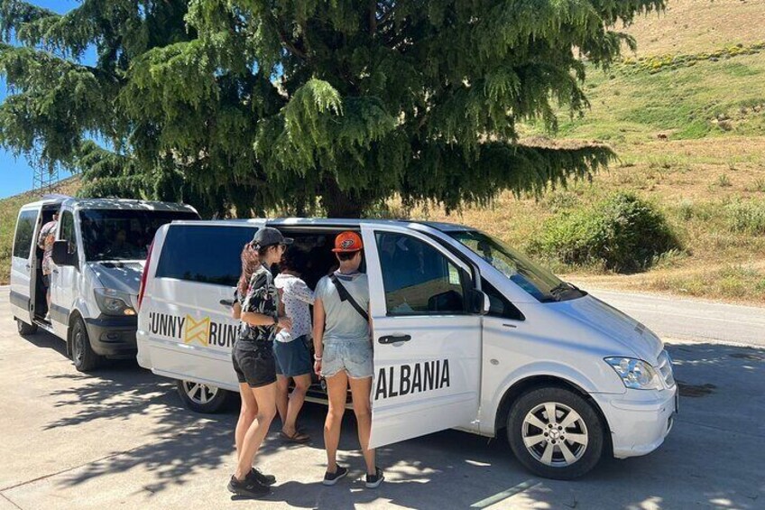 A white van with 'Sunny Run Albania' written on it, parked on a road with a person standing next to it. 4
