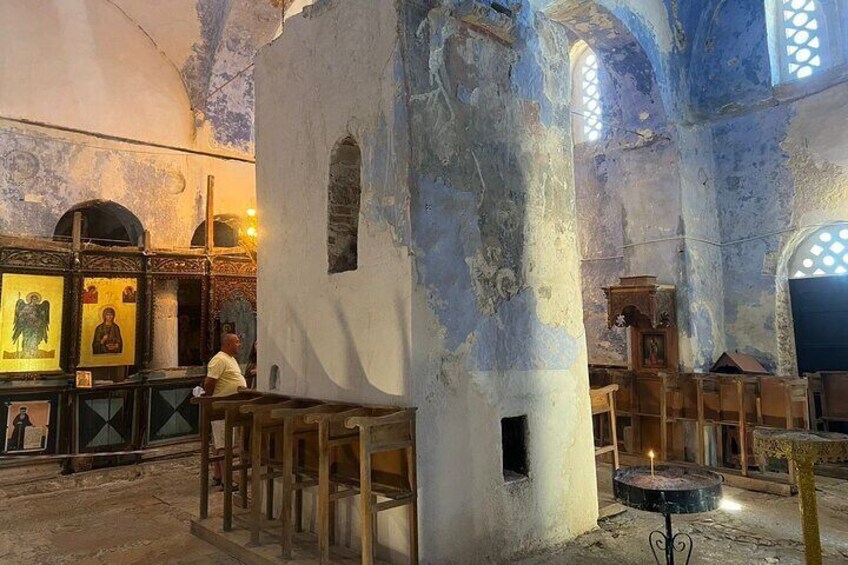 An interior of a church with wooden benches, a central pillar, and religious icons on the walls. 2