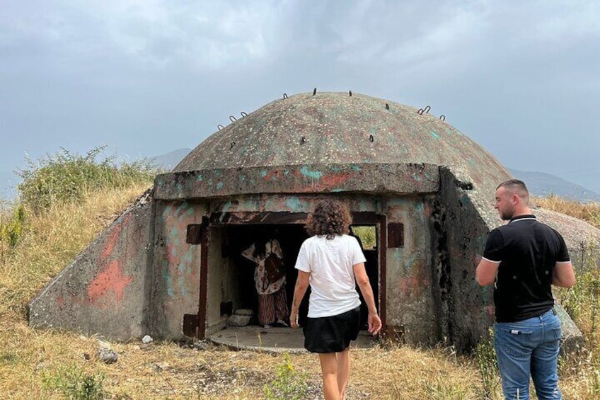 Una struttura arrugginita a forma di cupola con un'apertura, circondata da erba secca e colline. 4
