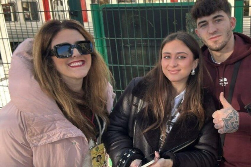 Three people posing in front of a green metal fence. 2