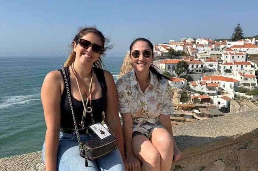 Two people sitting by the sea with a coastal town in the background. 1