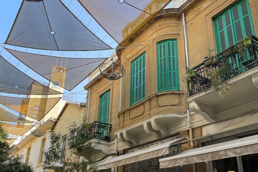 Un edificio con contraventanas verdes, balcones con plantas y sombrillas grandes. 3