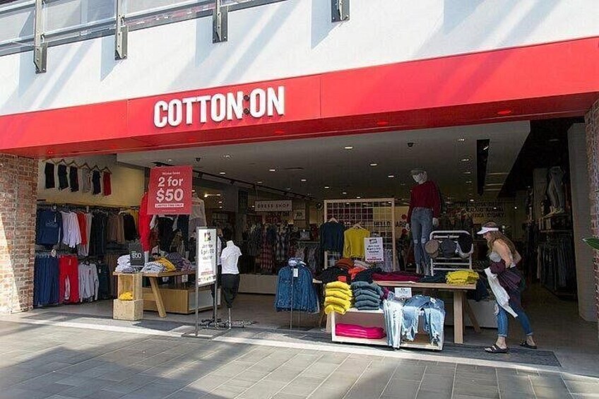 A clothing store named Cotton On with a red awning, a sale sign, and mannequins displaying clothes. 2