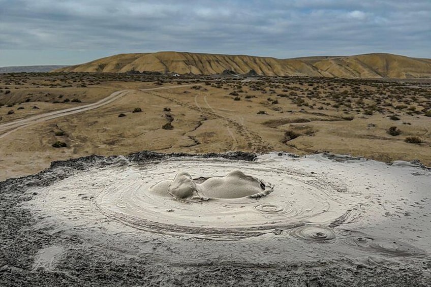 Woestijnlandschap met een grote, ronde zandstructuur en heuvels in de verte. 5