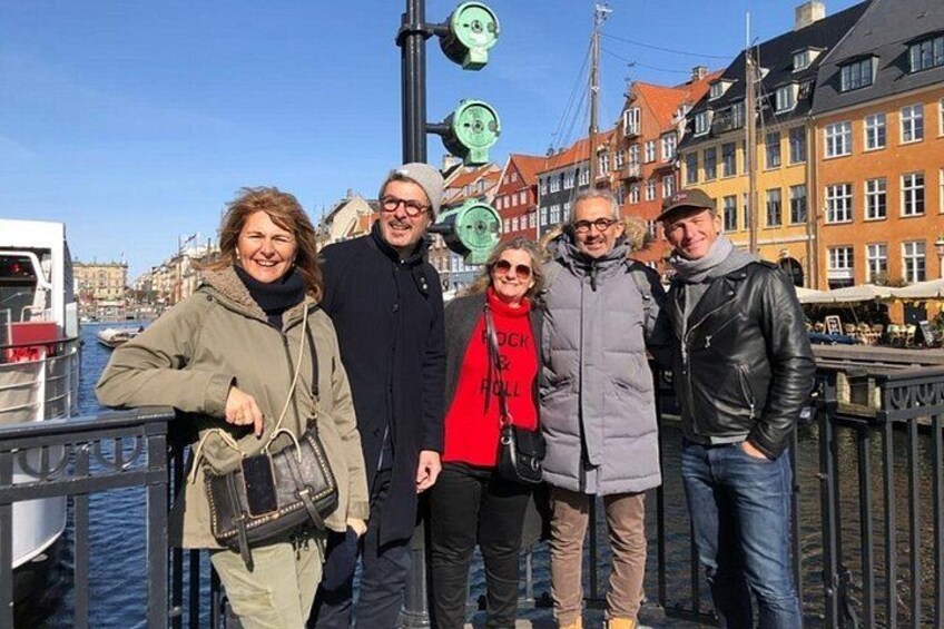 Een groep mensen staat bij een gracht, met gebouwen op de achtergrond. 2