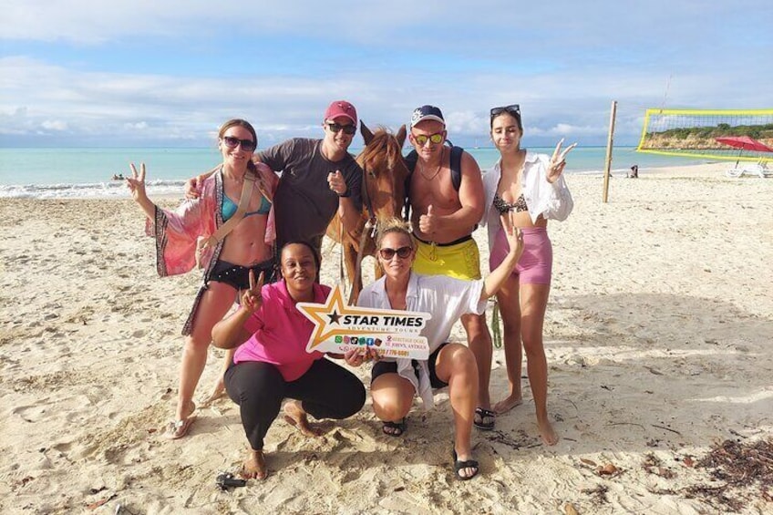 A group of people posing on a sandy beach with a volleyball net in the background. 1