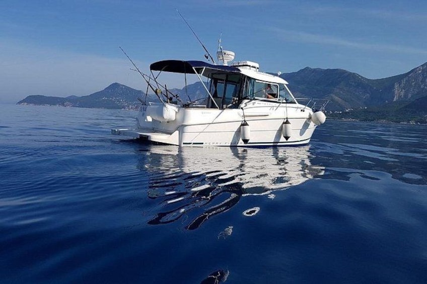 En hvid båd med fiskestænger på vandet, med bjerge i baggrunden og stille vand. 2