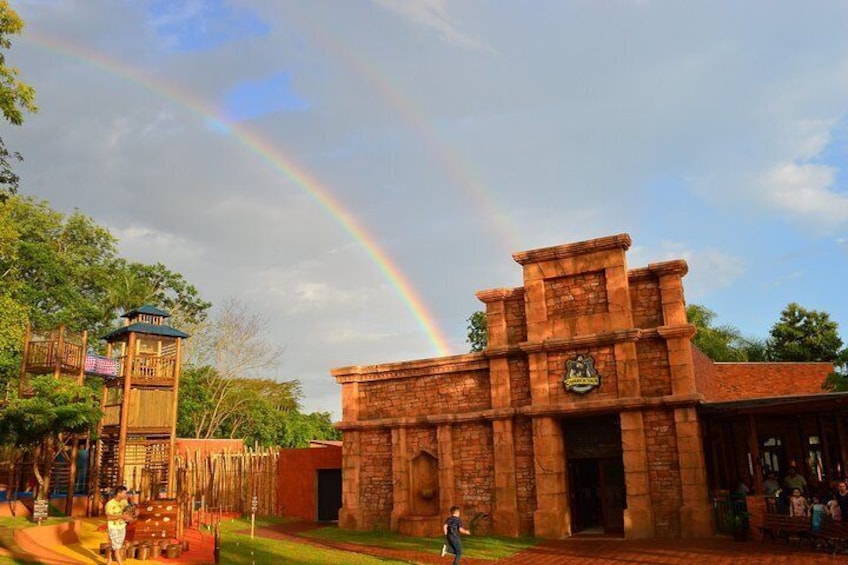 A brick building with a crest, a wooden structure with a flag, and a rainbow in the sky. 4