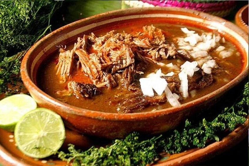 A traditional clay bowl filled with a stew, garnished with onions and lime wedges. 1
