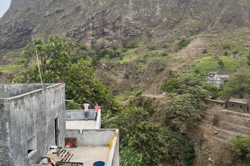 Ländliche Landschaft mit einem Betongebäude, einer Person auf einem Dach und einem Tal mit terrassenförmig angelegten Feldern. 3