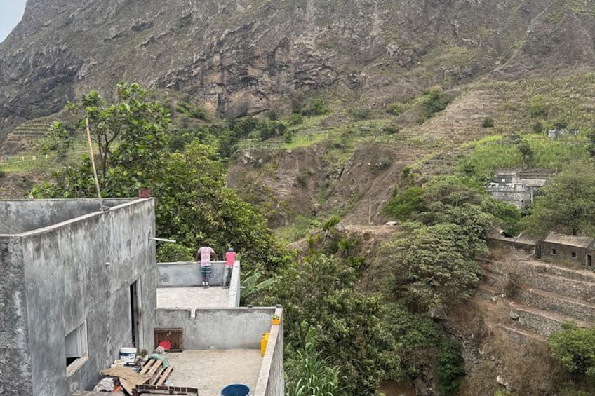 A rural landscape with a concrete building, a person on a rooftop, and a valley with terraced fields. 3