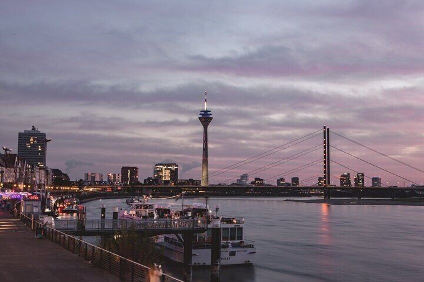 Ein Stadtbild im Abendlicht mit einem markanten Turm und einer Hängebrücke. 1