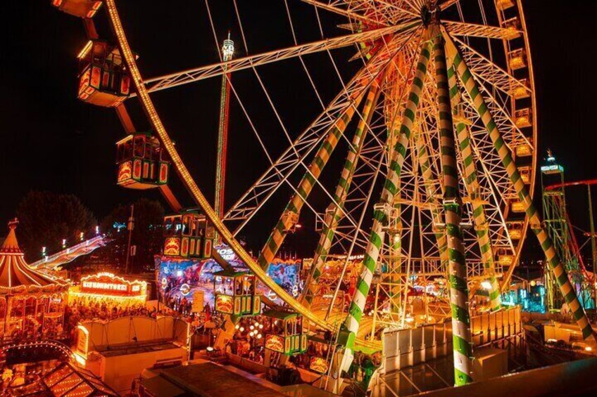 Ein großes Riesenrad bei Nacht mit bunten Lichtern und ein Karussell in der Nähe. 2