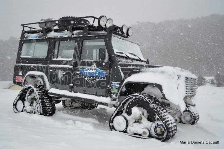 A snow-covered vehicle with tracks, a logo, and a snowy landscape. 4
