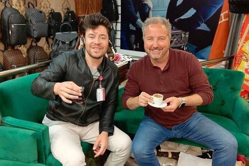 Twee personen zitten op een groene bank, één met een kopje en de ander met een bord. 2