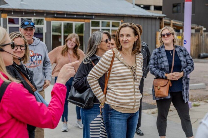 A group of people walking on a sidewalk, some carrying bags, with a building in the background. 3