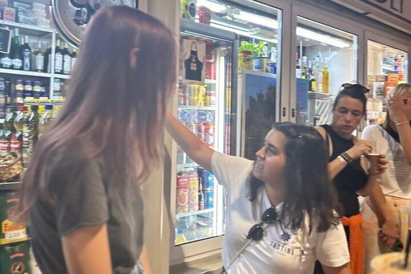 Una persona con cabello largo, una tienda con estantes llenos de diversos productos y otras personas al fondo. 3