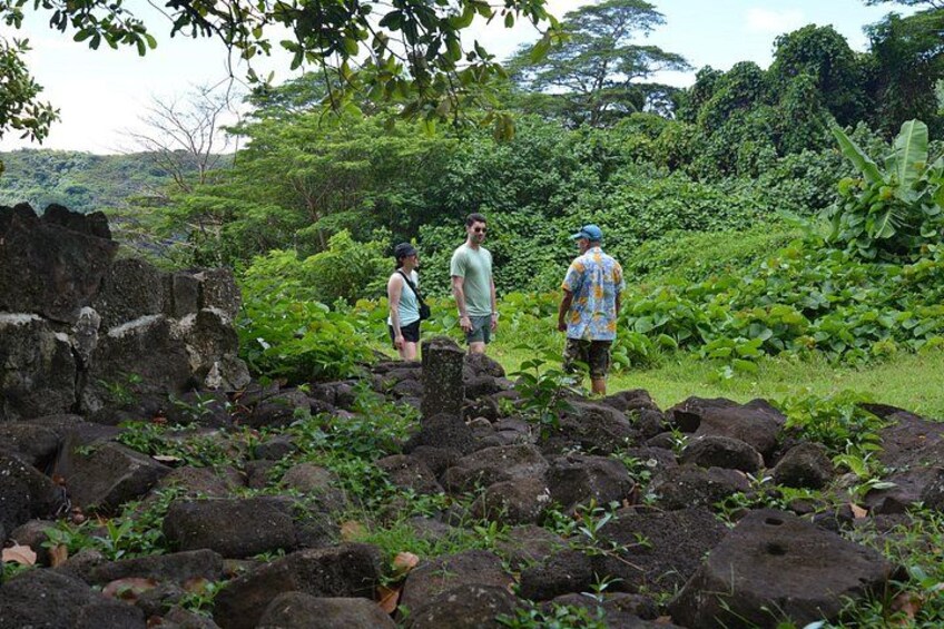 Tre persone che camminano su un sentiero circondato da vegetazione lussureggiante e grandi rocce. 3