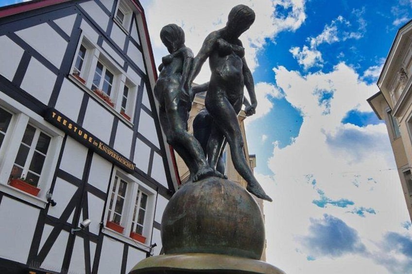 A statue of two figures on a pedestal in front of a building with a sign that reads 'TEESTUBE IN KNUFFERLAUEN.' 4