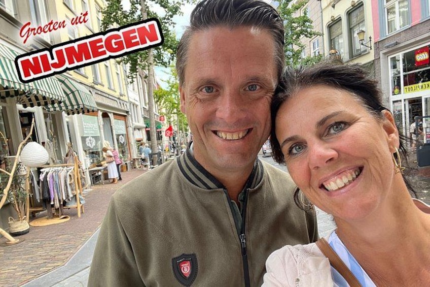 A couple in a street with shops and a sign that reads 'Groeten uit NIJMEGEN'. 5