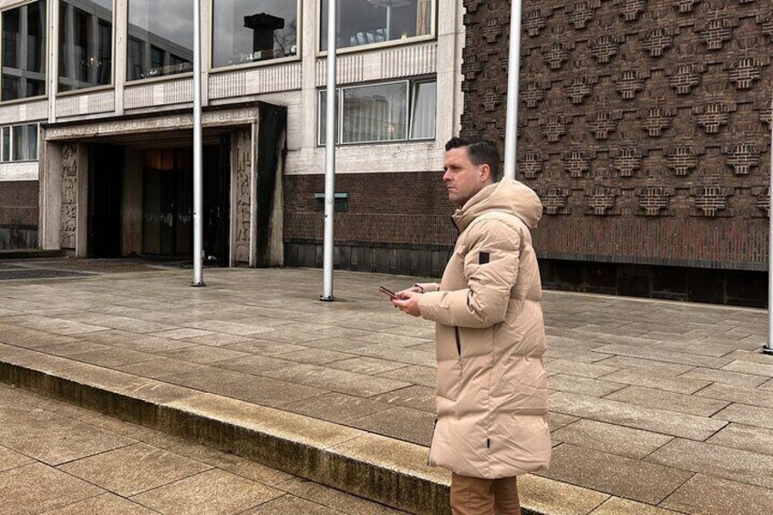 A person standing on a paved sidewalk in front of a building with a patterned facade. 4