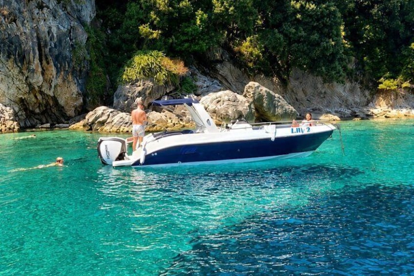 A boat with people on it, clear blue water, and rocky cliffs in the background. 1