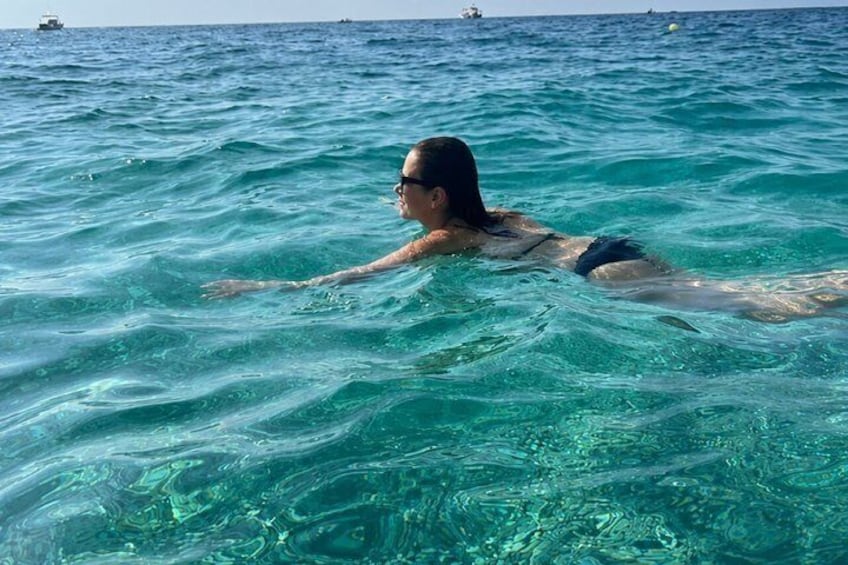 A person swimming in clear blue water with a boat in the distance. 3