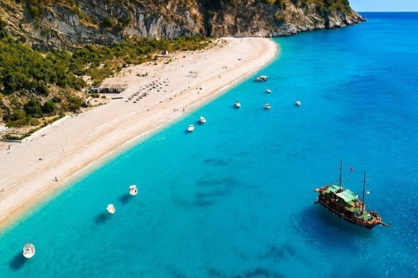 A coastal beach with clear turquoise waters, a sandy shore, and several boats anchored near the beach. 5