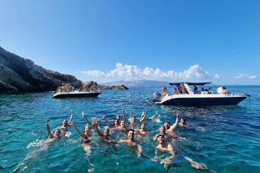 A group of people swimming in clear blue water with boats in the background. 2