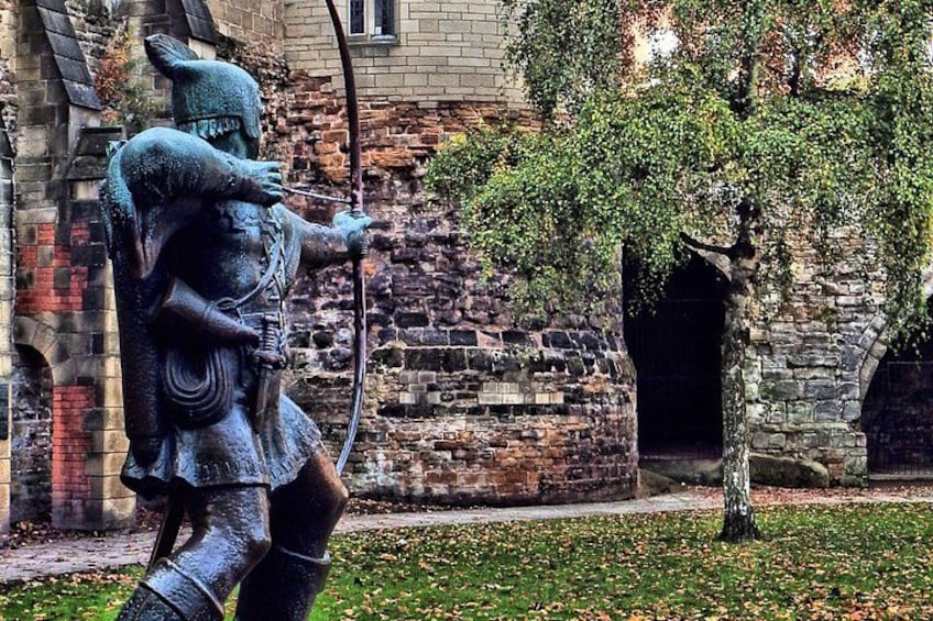 A statue of a figure with a bow and arrow, a stone building, and a tree in the background. 4