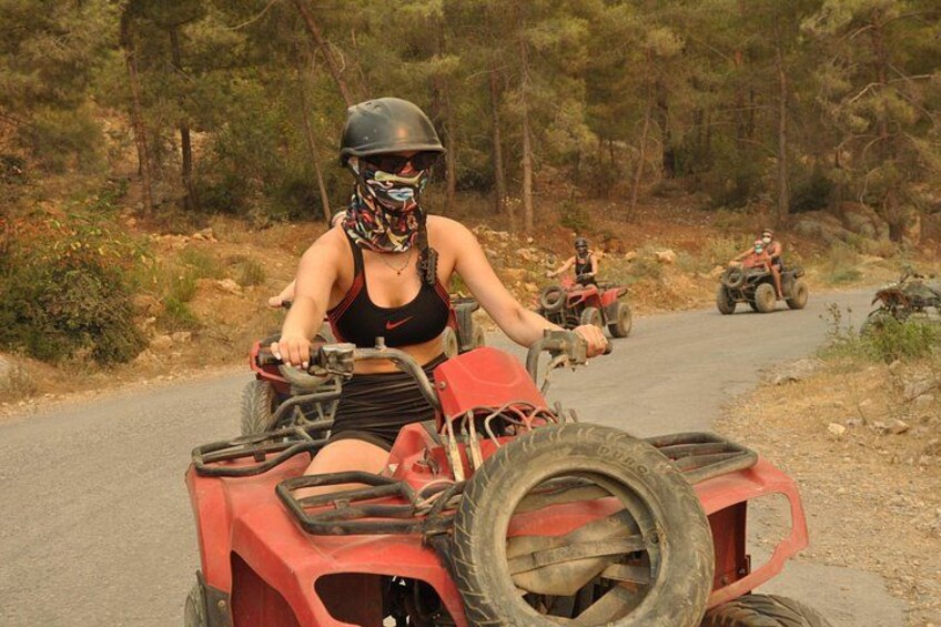 En person kører på en rød ATV på en asfalteret vej med træer i baggrunden. 2
