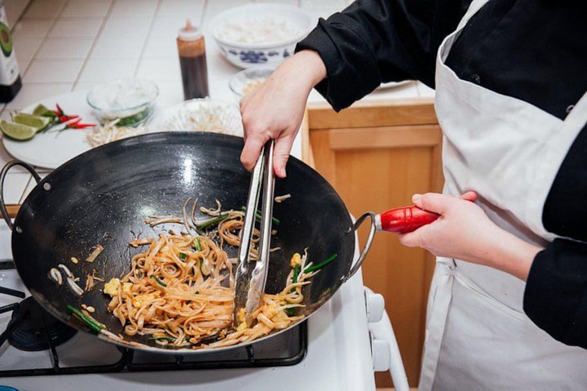 A person cooking noodles in a wok on a stove. 2