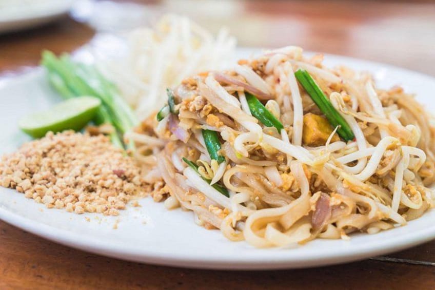 A plate of Pad Thai noodles with bean sprouts, green onions, and lime wedges. 3