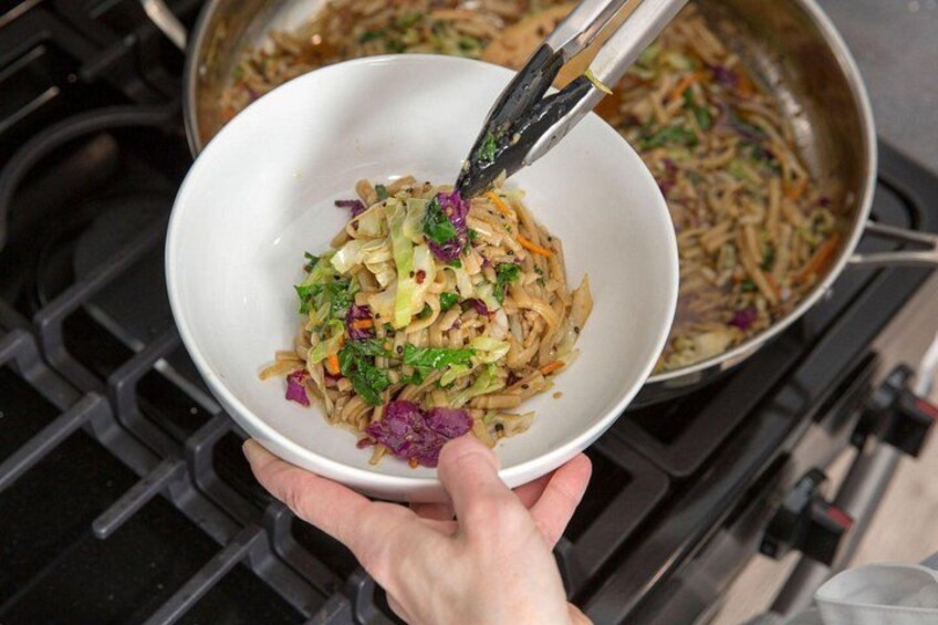 A person holding a bowl of stir-fried noodles with vegetables. 4