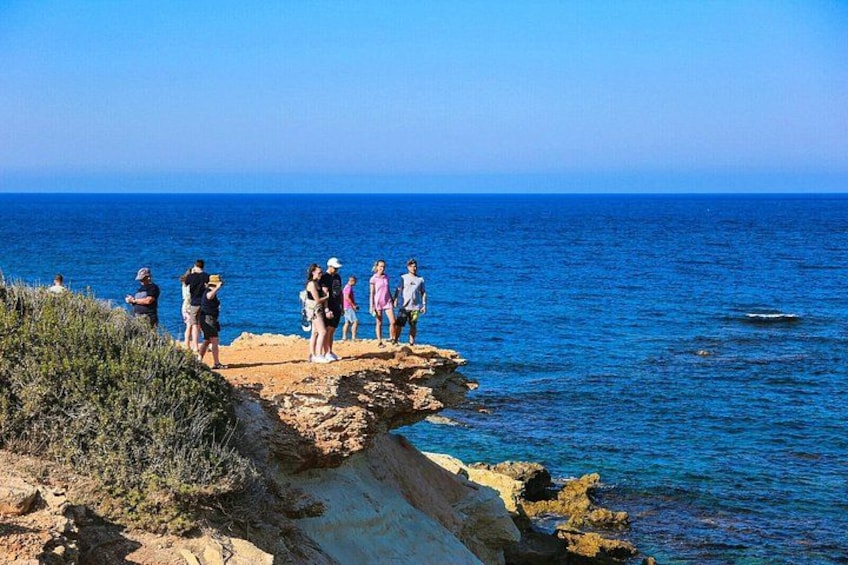 A group of people standing on a rocky cliff overlooking the sea. 3